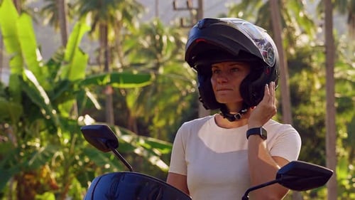 Young Woman Sitting on Scooter Lowering Internal Helmet Sun Visor While Looking at Tropical Road Wit