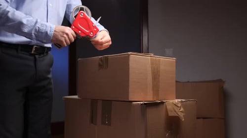 Man Sealing Cardboard Boxes with Tape Gun Indoors