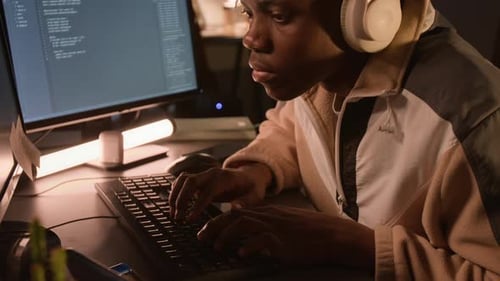 Black Man Wearing Headphones Programming Software on Computer at Night