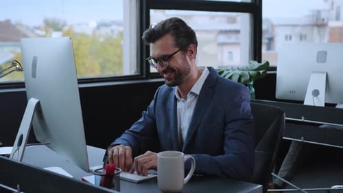A Professional Man Sits at His Desk Diligently Working on His Computer in a Modern Office Setting