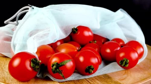 Apila jugosos tomates cherry frescos en una bolsa de malla ecológica que gira suavemente