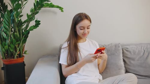Woman Using Smartphone Relaxing on Couch at Home