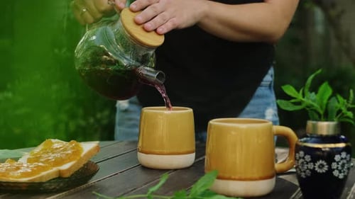 Outdoor Tea Party Woman Pouring Red Herbal Tea Into Mug on Wooden Table
