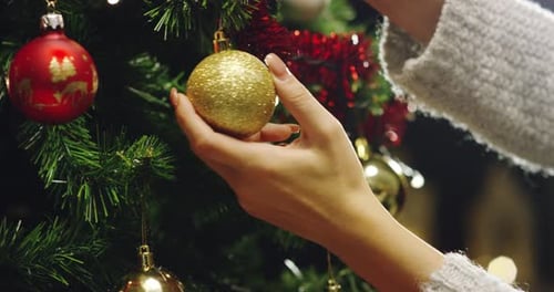 Woman Hand Decorating Christmas Tree with Gold Ornaments