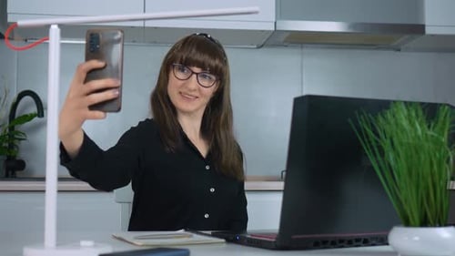 Businesswoman Remote Working Online Sitting at Kitchen Table Using Laptop and Taking Selfies on