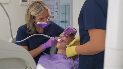 Female dentist with assistant working in dental clinic examining patient teeth.