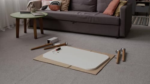 Outils d'assemblage, y compris un tournevis, un plateau de table blanc et des pieds en bois sur tapis