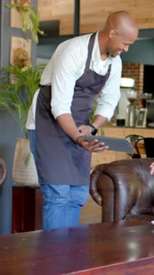 Vertical video: Approaching server showing tablet to patron at cafe in dark apron confirming order