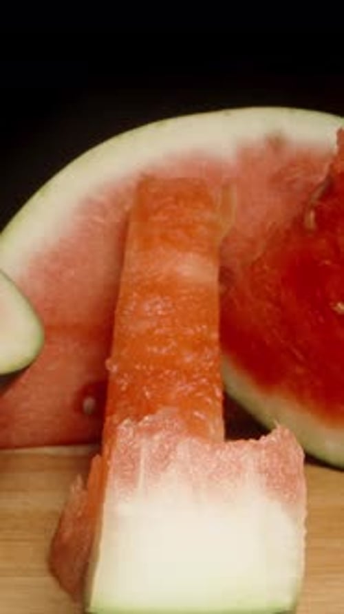 Vertical video. A gnawed watermelon rind on a wooden table with intact pieces, dolly shot, close-up.