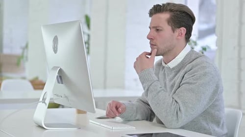 Creative Young Man Thinking and Working on Desktop