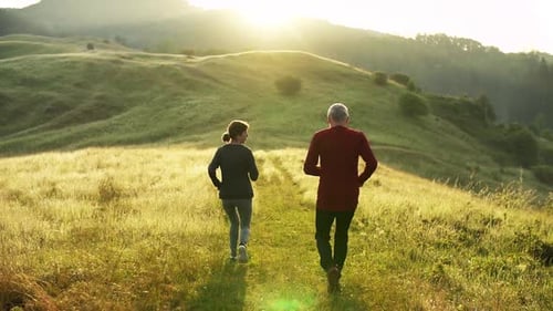 Rear View of Senior Sporty Couple Running on Meadow in Nature At