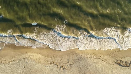 Vertical shot of the waves crashing on the beach. Beautiful green turquoise water with sandy beach.