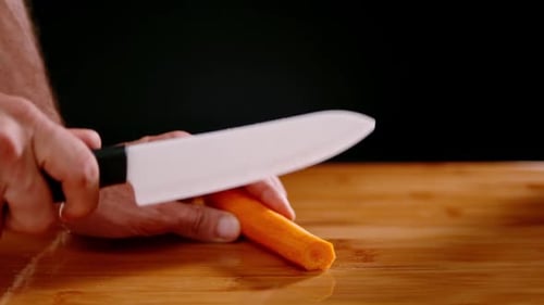 Cutting orange carrot with sharp chef knife, slow motion view