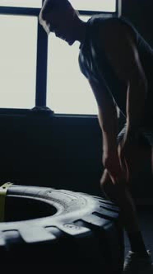 Man Performing Tire Lift Exercise in Dark Gym for Strength Training