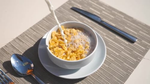 Detail View on Stream of Fresh Milk Pouring Into Bowl with Dry Crispy Cornflakes