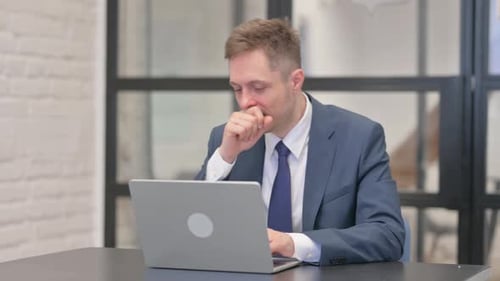 Man in Suit Coughs While Working on Laptop
