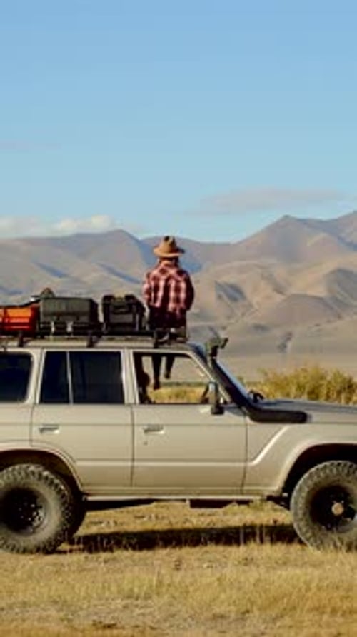 Adventurer Standing on Car Roof in Desert Landscape