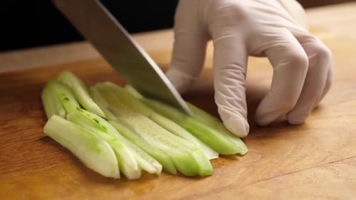 Hand Slices Green Vegetable Stems on Board