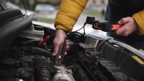 Driver Connecting A Jump Starter Battery To Car Engine