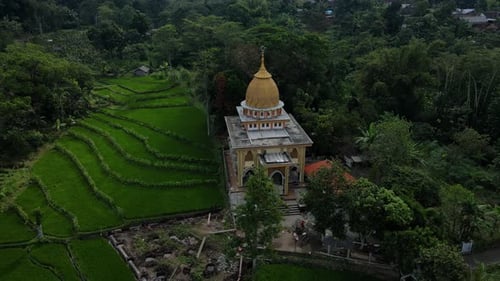 4K drone footage of a golden dome mosque surrounded by lush forests and rice fields. The stunning ae