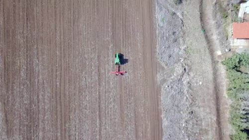 Green Tractor cultivating and seeding a dry field - Top down aerial footage