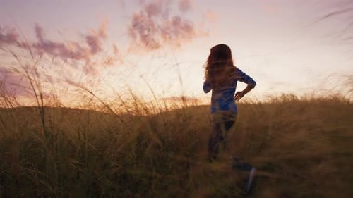 Mujer entra corriendo en el campo de verano con hierba y plantas silvestres al atardecer