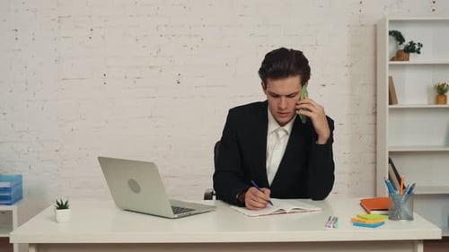 Man in Suit Talks on Phone and Writes