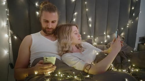 Couple Relaxing in Bed, Looking at Smartphones