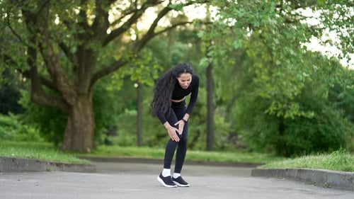 Young woman suffers from painful severe knee joint ache during a morning run in urban city park.