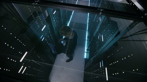 Vista desde arriba a través del cristal de un ingeniero de TI que trabaja con un portátil en un centro de datos lleno de Active Rack S