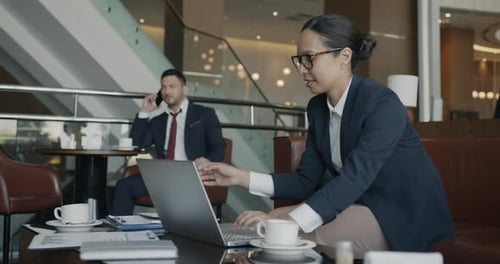 Cheerful Businesswoman Speaking on Mobile Phone and Working with Laptop in Hotel Hall