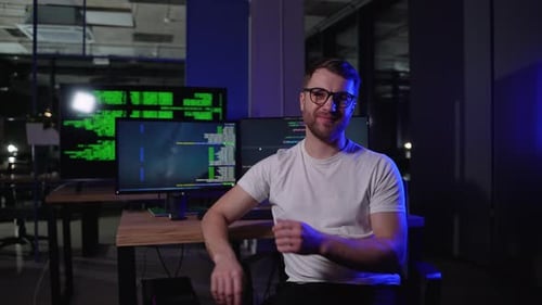 Portrait Of Programmer In Dark IT Office Sitting At Desk