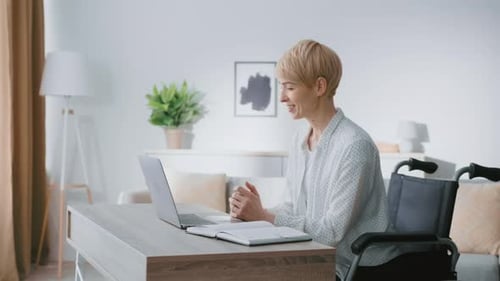 Mujer usando una computadora portátil en una habitación moderna con planta y silla de ruedas durante el día