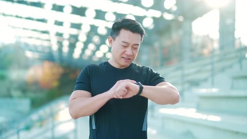 Sport asian man looking smart watch at modern track. Man runner using smartwatch bracelet. Portrait