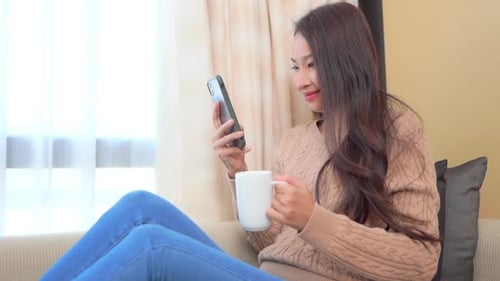 Woman Relaxing on Sofa with Smartphone and Coffee