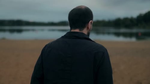 Lonely Man Walks By Lake Under Moody Sky Back View of Solitude
