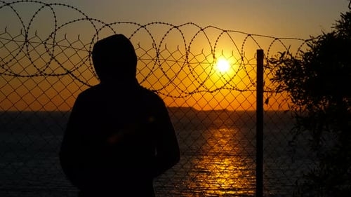 Young Man Contemplating Sunset Behind Barbed Wire Fence