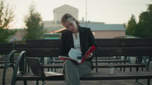 Young Woman Reviews Documents Outdoors on Bench