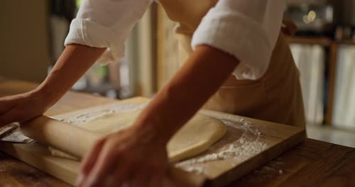 Close Up of a Girl Baker in a White Shirt and a Beige Apron is Rolling Out the Finished Dough Using