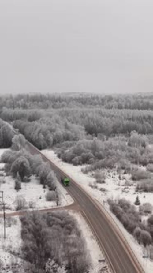 Vertical aerial view of a two lane highway in countryside with truck passing by on a cloudy winter d
