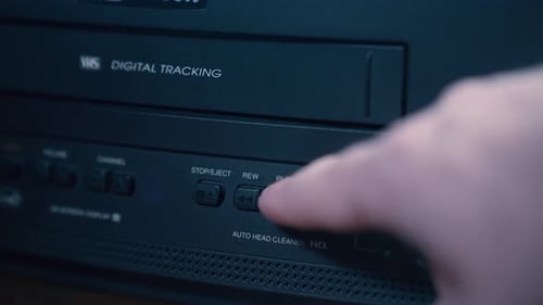 Finger Pressing Rewind Button on Black VCR