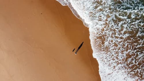 Luftaufnahme von oben nach unten einer Person, die sich am Sandstrand ausruht und vor starken Meereswellen Angst hat
