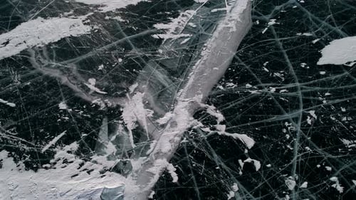 Aerial Tilt Shot of Cracked Blue Ice and Cape Khoboy Olkhon Island Tall Rocks in Frozen Lake Baikal