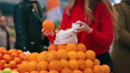 Mujer recogiendo naranjas en una bolsa reutilizable en una tienda. Temáticas del Día de la Tierra y la Ecología