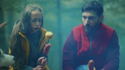 Face Family Sit Around a Campfire on Autumn Evening in the Woods Frying Sausages Over a Fire in