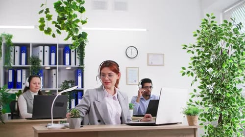 Young Woman with Microphone and Headphones Working As Call Center Operator with Her Colleagues in