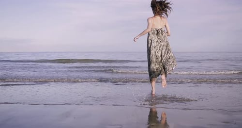 Young adult woman running into the sea in dress