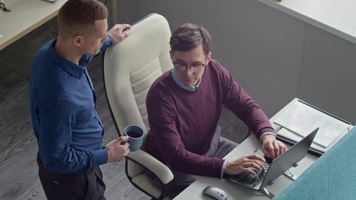 Two Male Colleagues Discussing Job while Looking at Laptop at Office