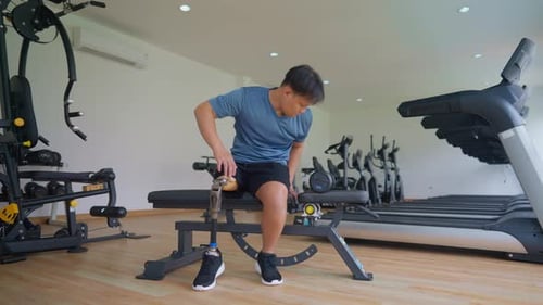Asian young man with a prosthetic leg lifts a dumbbell at the gym.