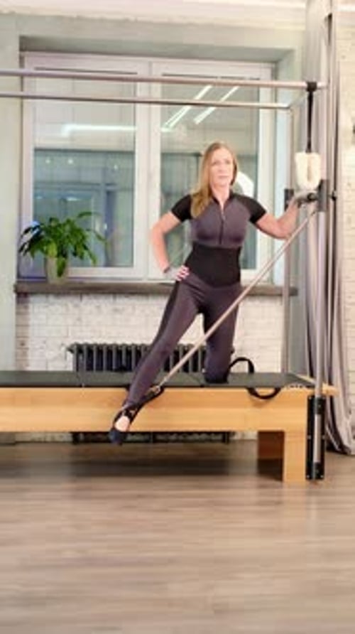 A Woman Performs a Pilates Leg Extension Exercise on a Reformer Tower Maintaining Posture and